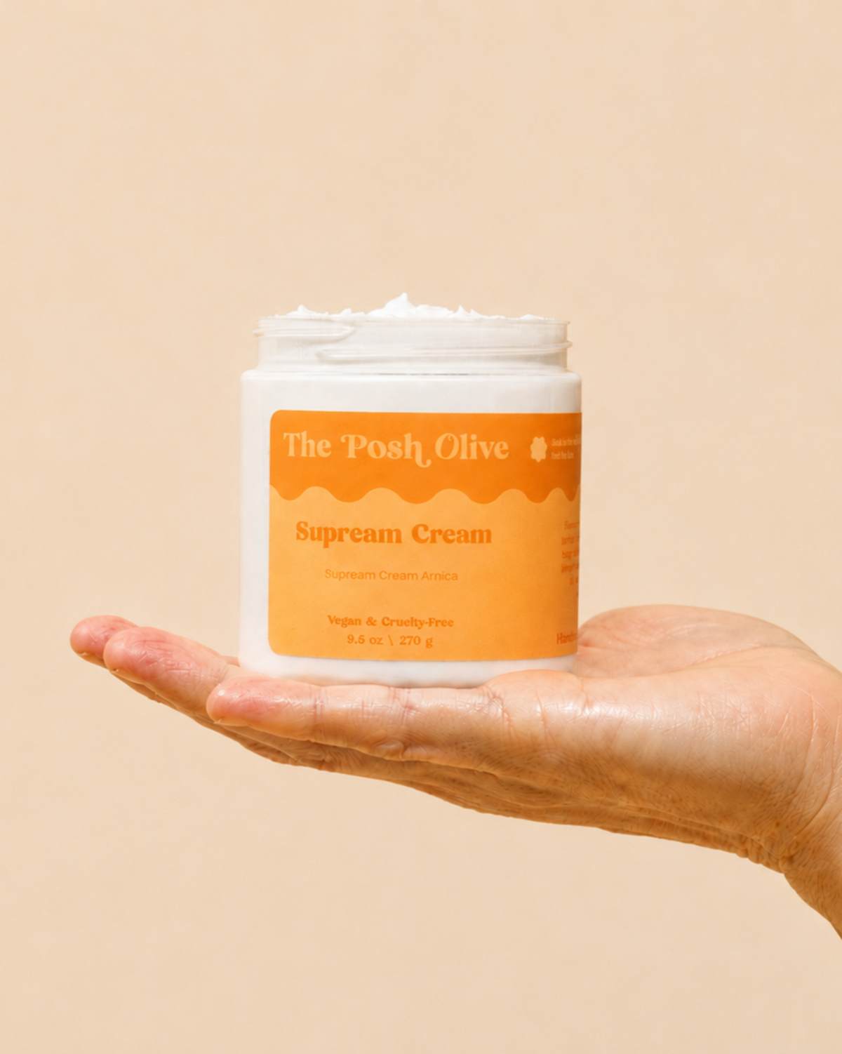 The Posh Olive Supreme Cream with arnica in open jar held in hand